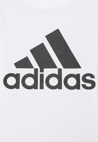 Witte T-shirt met een groot zwart Adidas-logo, met daarboven drie diagonale strepen en de merknaam in vetgedrukte hoofdletters.