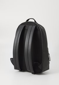 Black backpack with mesh back panel and padded shoulder straps. Features a zipper and a small label side accent. Smooth texture overall.