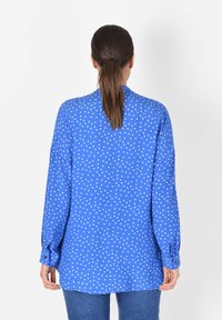 Blå långärmad skjorta med vita prickar, knappmanschetter och rak fåll. Tillverkad av ett mjukt material med en avslappnad passform.