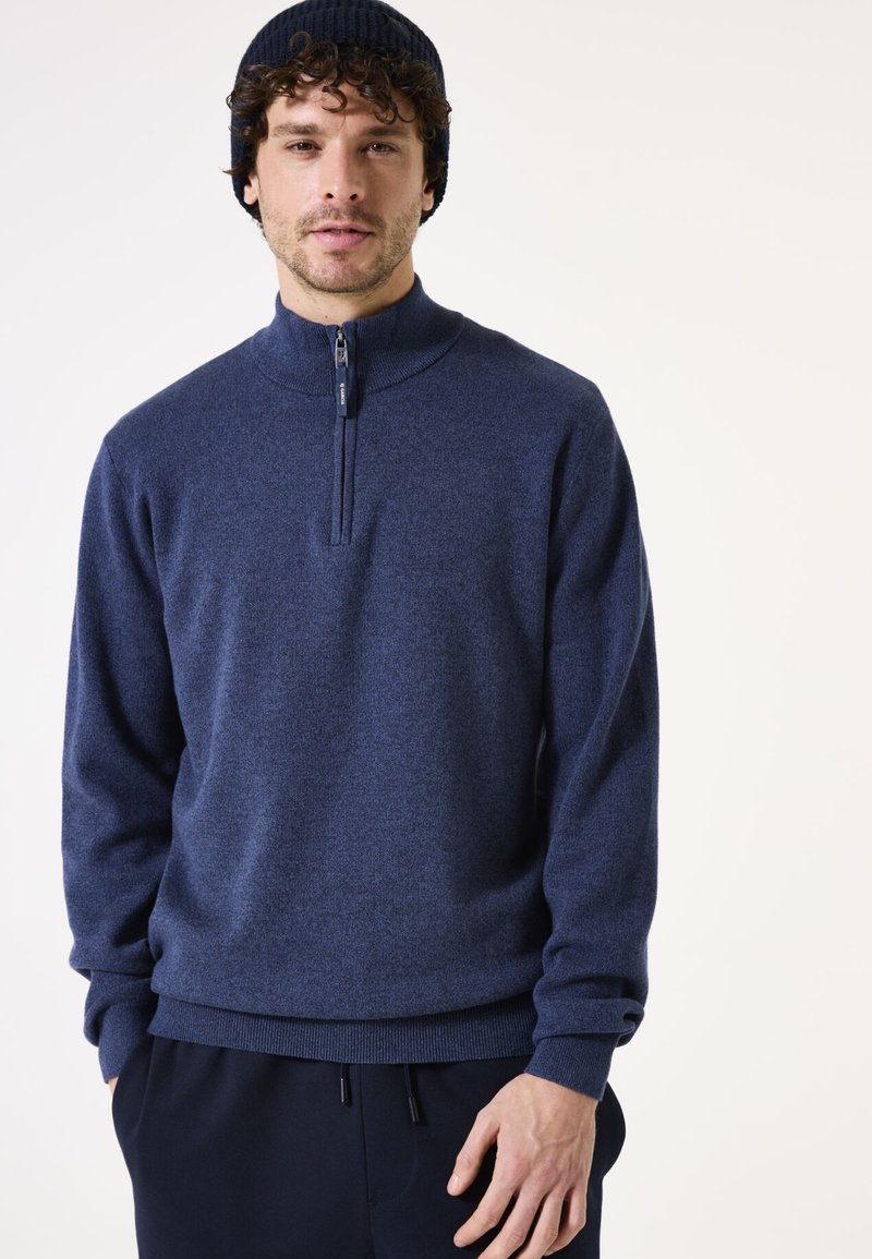 Marineblauwe half-zip trui met een gestructureerde brei en geribbelde mouwen. Draag met donkere broeken, handen in de zakken.