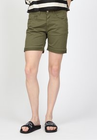 Olivgröna uppvikta shorts med framfickor, metallknäppning och kontrasterande svarta sandaler med vit text.