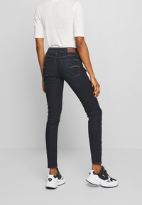 Tunna mörkblå jeans med en slät yta, subtila sömmar och bakfickor. Tillsammans med vita och svarta sportskor.