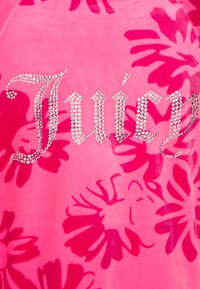 Roze velours top met een bloemenpatroon in een donkerdere tint roze. Het woord "Juicy" is versierd met strass steentjes.