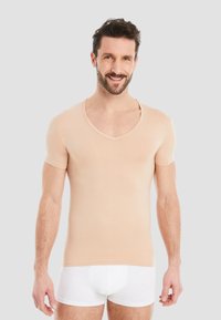 Beige fitted t-shirt with short sleeves and a deep V-neck. Soft fabric with a smooth texture. Worn with white underwear.