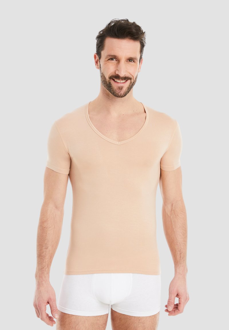 Beige fitted t-shirt with short sleeves and a deep V-neck. Soft fabric with a smooth texture. Worn with white underwear.