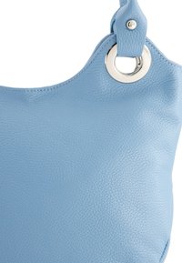 Lichtblauwe leren handtas met een gestructureerd oppervlak. Kenmerken zijn onder meer een cirkelvormige zilveren hardwareaccent en een schouderband die aan de tas is bevestigd.