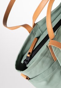 Groene stoffen draagtas met tan leren handvatten en accenten. Voorzien van een ritsluiting en zichtbare stikseldetails.