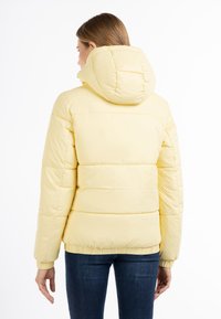 Gul pufferjakke med hætte, der har et quiltet design og elastiske manchetter. Glat tekstur og tætsiddende i taljen, strækker sig til hofterne.