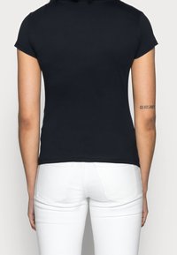 Námořnická modrá tričko s krátkým rukávem a přiléhavým střihem, vyrobené z bavlny, s klasickým výstřihem, v kombinaci s bílými džíny s kapsami na zadní straně.