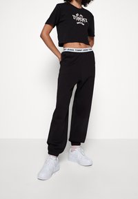 Černé zkrácené tričko s logem "TOMMY JEANS", spárované s černými tepláky s elastickým pasem a bílými akcenty. Bílé tenisky.