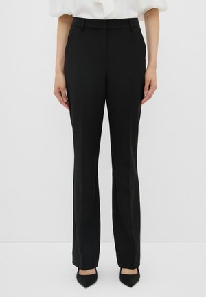 Pantalons noirs ajustés avec une jambe droite, fabriqués en tissu lisse. Dotés d'une taille et de passants de ceinture, associés à des talons aiguilles noirs.