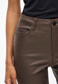 Hnědé kalhoty z umělé kůže s přiléhavým střihem, předními kapsami a hladkým, lesklým povrchem, které mají zapínání na knoflík a poutka na opasek.