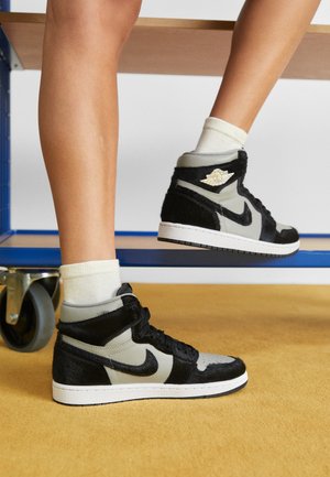 Jambes portant des chaussettes blanches et des baskets montantes noires et grises avec un logo Nike, reposant sur un banc métallique bleu avec roulettes.