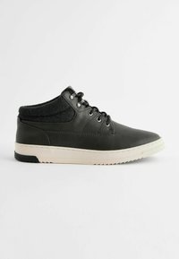 Zapatilla negra de cuero con un collar de tejido oscuro texturizado, cordones redondos y una suela de goma blanca con acentos negros y un patrón de tracción.