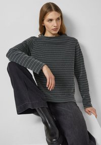 Czarnobiały sweter w wzory z długimi rękawami i luźnym krojem, zestawiony z ciemnymi szerokimi dżinsami i czarnymi botkami za kostkę.