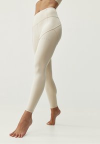 Leggings beiges taille haute en tissu lisse et extensible. Présentent des détails de couture minimalistes et un petit logo près de la cheville.