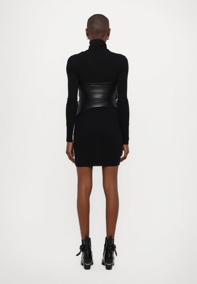 Haut noir à manches longues avec col montant, au design ajusté, associé à une robe mini noire et des bottines à talons hauts avec des accents de volants.