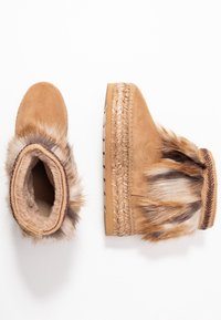 Tan mockasiner i nubuck med pälsdetalj och kilklackar, en sko vänd uppåt och den andra som visar sidan.