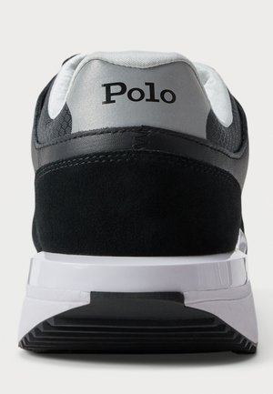 Takaa kuvattu musta ja harmaa tennari, jossa valkoinen pohja ja jonka harmaassa kantapään kielekkeessä lukee "Polo".