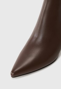 Chaussure à talon haut en cuir marron avec un bout pointu et une texture lisse, au design épuré et minimaliste.