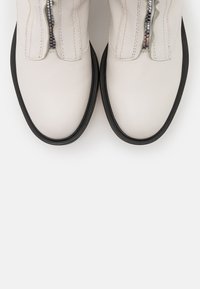 Botas de tobillo de cuero blanco con forma redondeada, suela de goma negra en contraste, cremallera vertical y detalles de costura visibles.