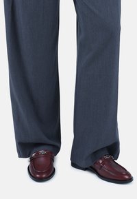 Los mocasines de cuero marrón presentan un diseño sencillo con un acento de cadena, combinados con pantalones de pierna ancha en gris oscuro, fabricados con una tela suave.