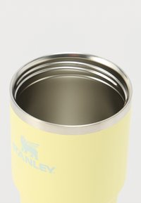 Gobelet en acier inoxydable jaune avec une texture lisse, bordure argentée et un logo discret près de la base. Le dessus ouvert révèle la doublure intérieure.