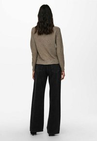 Brauner Strickpullover mit langen Ärmeln und abgerundetem Saum, kombiniert mit hochtaillierten, weit geschnittenen schwarzen Jeans, die über Gesäßtaschen und sichtbare Nähte verfügen.