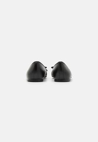 Zapatos planos de cuero negro con punta redondeada, tacón plano y detalle de costura mínima en la parte trasera. Textura suave, diseño aerodinámico.