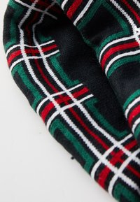 Tessuto nero con un motivo tartan che presenta linee verdi, rosse e bianche. Morbida texture con un bordo arrotondato, piegato parzialmente.