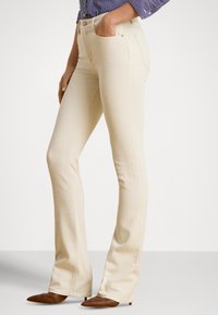 Jeans cor de bege com corte a sino, feitos de ganga macia, com bolsos frontais, cintura ajustada e detalhes sutis de costura.