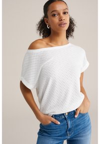 Balta trumpomis rankovėmis palaidinė su laisvu siluetu ir nusmukusiom petnešom, su tekstūruota žuvies kaulų raštu ir suvyniotomis rankovėmis.