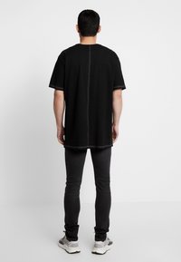 Svart överdimensionerad t-shirt med kontrasterande sömmar, korta ärmar, rak skärning och en söm nedtill i mitten av ryggen, i kombination med mörka jeans.