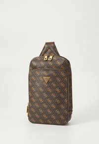 Barna designer oldaltáska aranyszínű cipzárokkal, monogrammintával és első zsebbel, egyszerű világos háttér előtt.