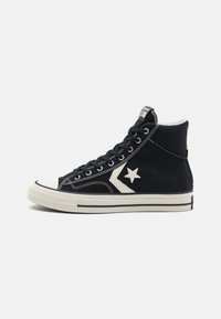 Zapatillas de caña alta negras hechas de lona, con una puntera de goma blanca, un logo de estrella en contraste y detalles de costura blanca.