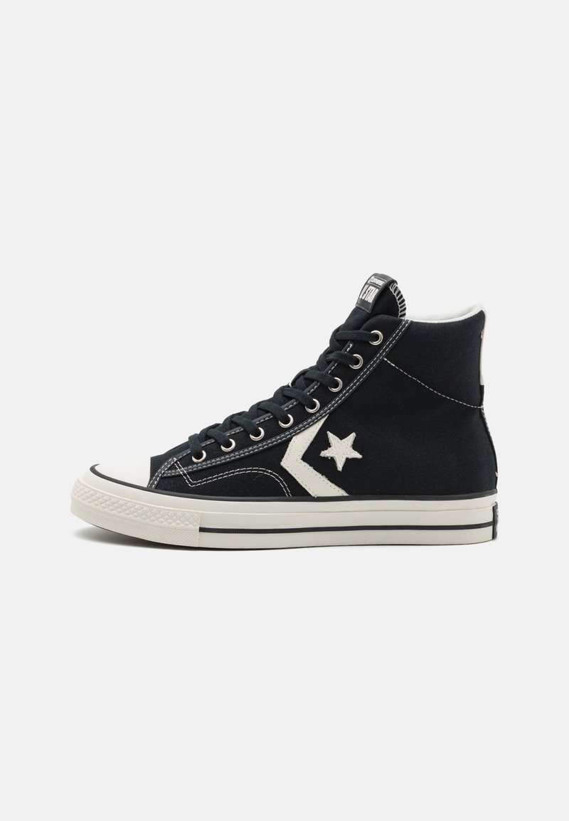Zapatillas de caña alta negras hechas de lona, con una puntera de goma blanca, un logo de estrella en contraste y detalles de costura blanca.