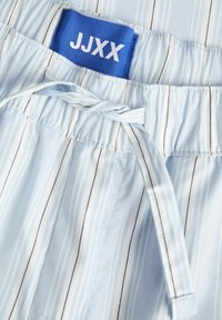 Svijetloplave kratke hlače s trakicama u struku, s plavom etiketom s bijelim tekstom. Tkanina ima glatku teksturu.