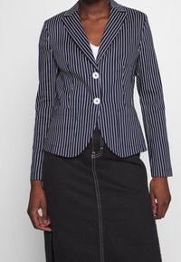 Blazer marine à rayures avec une coupe ajustée, deux boutons blancs, revers pointus et poches latérales ; en matière mélangée coton, texture lisse.