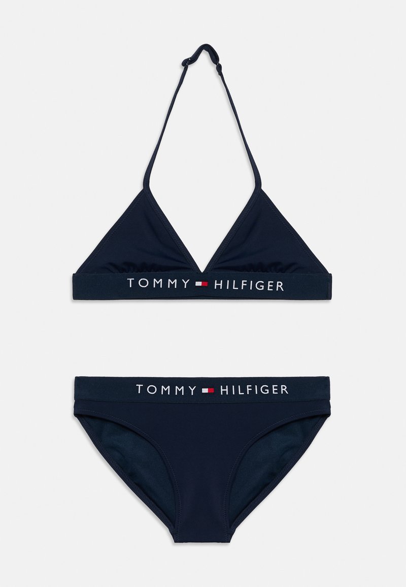 Μπλε σκούρο μπικίνι σετ δύο τεμαχίων με τοπ σε σχήμα τριγώνου και ρυθμιζόμενους ιμάντες, καθώς και κάτω μέρος με κορδέλα μέσης που φέρει λογότυπο σε αντίθετο χρώμα. Λεπτή υφή.