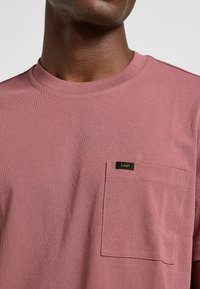 Kortärmad t-shirt med rund halsringning i rosafärg. Har en bröstficka på vänster sida och en liten svart etikett med "Lee" på. Mjuk bomullskvalitet.