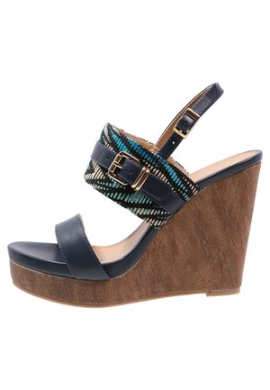 Marineblå kilehælssandaler med hæl med korklignende tekstur, glat lædersål og strop i mønstret stof med metalliske spændeaccenter.
