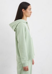 Lichtgroene hoodiesweater van zachte stof, voorzien van een voorzak, geribbelde manchetten en een losse pasvorm. Gestyled met bijpassende broek.