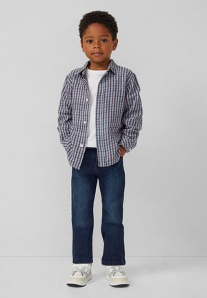 Gekruist button-up shirt in blauw en bordeaux, gecombineerd met een wit t-shirt en donkerblauwe jeans. Witte sneakers met grijze accenten.