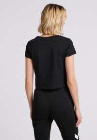 Camiseta negra recortada de manga corta, con cuello redondo y una textura suave, combinada con pantalones negros a juego.