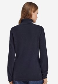 Mörkblå polotröja i mjukt stickat material, med långa ärmar och ribbad halsringning. Slät textur med minimal detaljering.