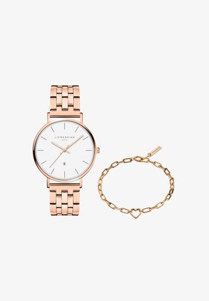 Roseguld armbåndsur med hvid urskive og minimalistisk design ved siden af en matchende kædearmbånd med et hjerteformet led og lås.