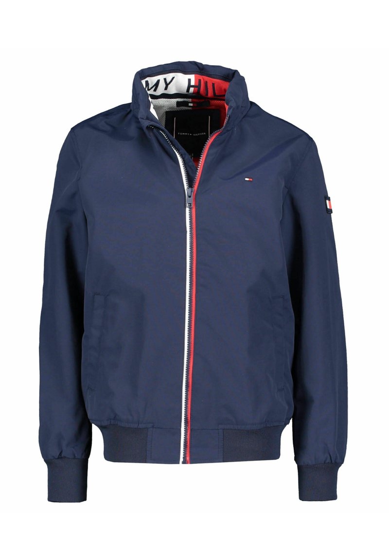 Dunkelblaue, leichte Jacke mit Stehkragen, Reißverschluss, roten und weißen Akzenten sowie elastischen Bündchen und Saum. Mit Logo auf dem Ärmel.