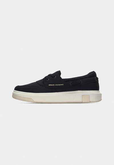 Baskets basses noires avec semelle blanche, laçage à l'avant, lettrage doré "Armani Exchange" sur le côté et détail texturé au talon.