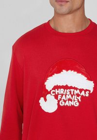 Camiseta roja de manga larga con un gran gráfico de un gorro de Santa acentuado en blanco y el texto "CHRISTMAS FAMILY GANG" en letras juguetonas y en negrita.