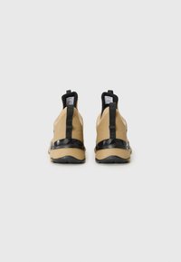 Tan and black athletic shoes with elastic panels, rubber soles, and pull tabs. Features a matte finish and minimal branding on the heel.